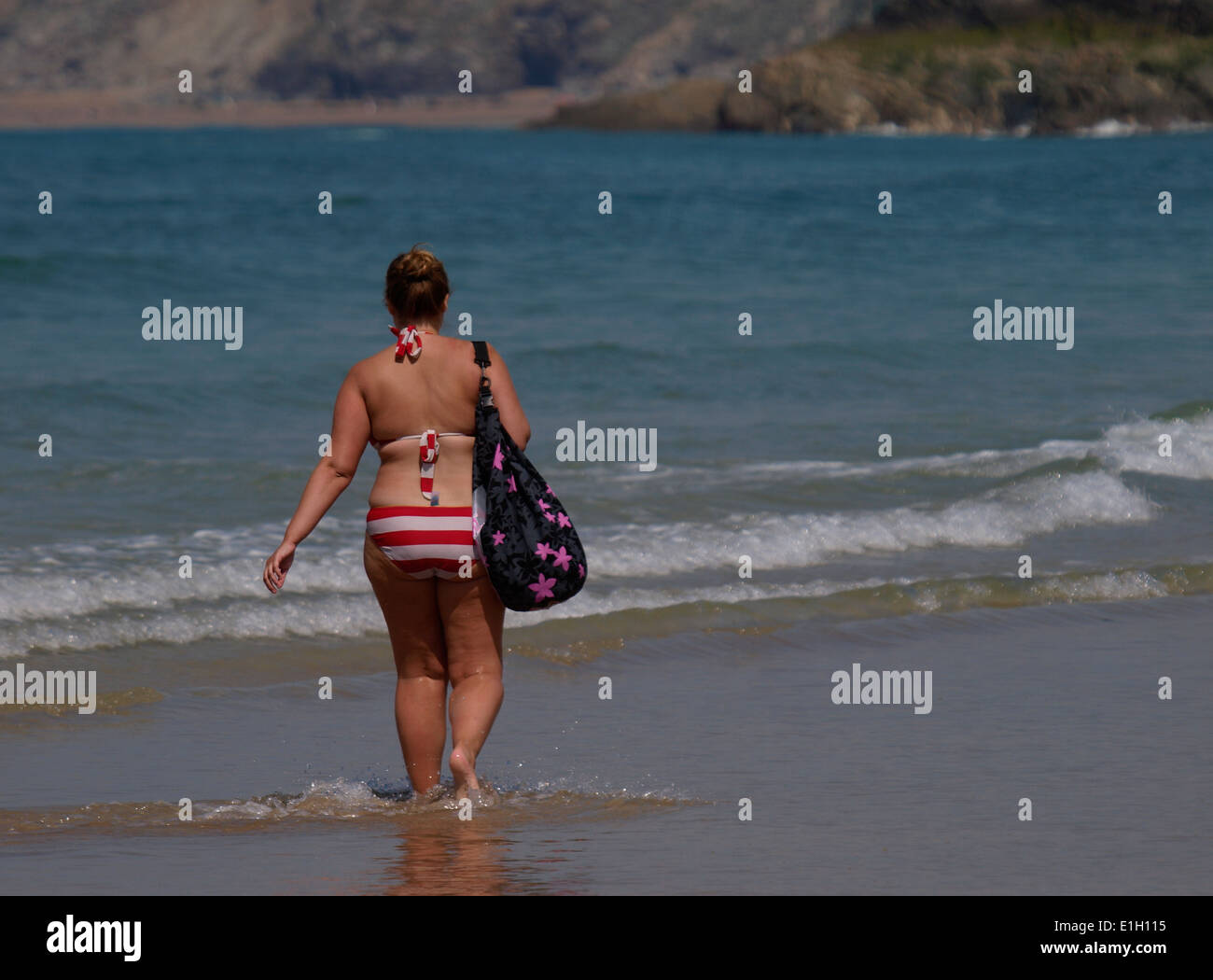 Sopra il peso donna paddling in spiaggia, Newquay, Cornwall, Regno Unito Foto Stock