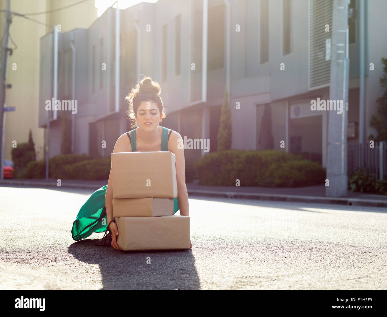 Giovane donna accovacciata per sollevare la pila di scatole di cartone Foto Stock