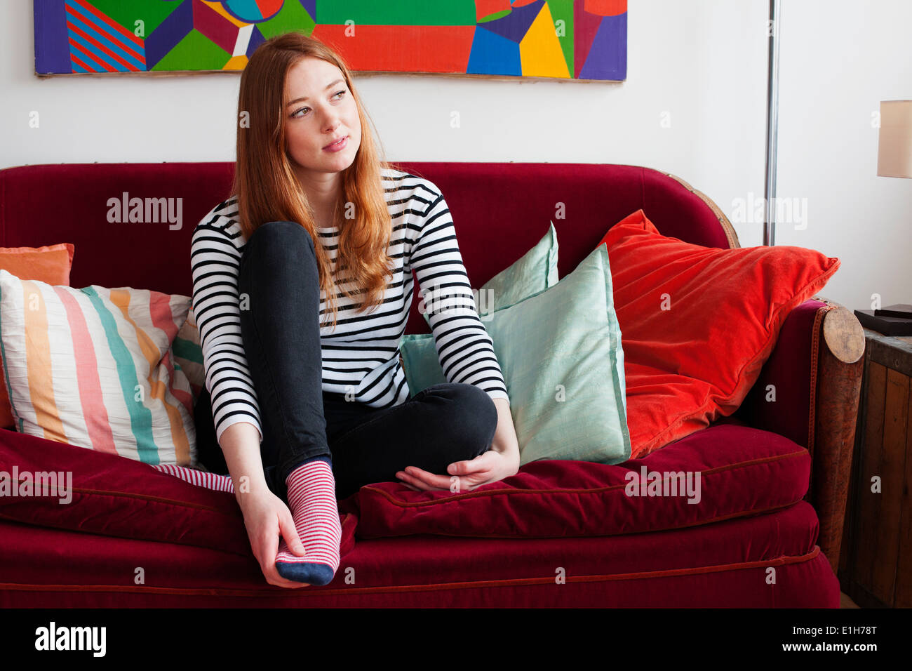 Giovane donna seduta su un divano con piedi Foto Stock