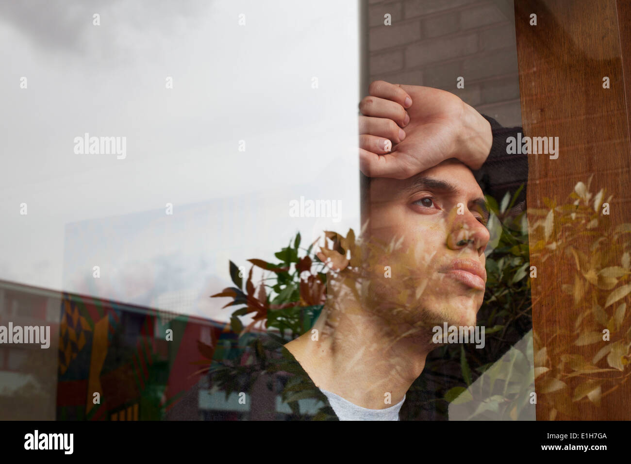 Giovane uomo con la mano sulla testa, guardando attraverso la finestra Foto Stock