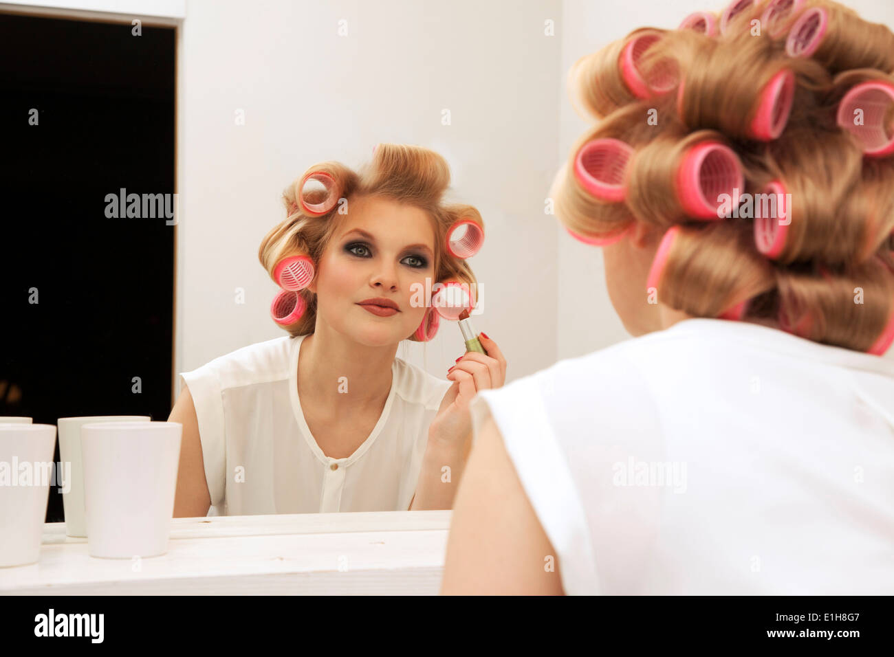 Giovane donna in bigodini mettendo sul make-up Foto Stock