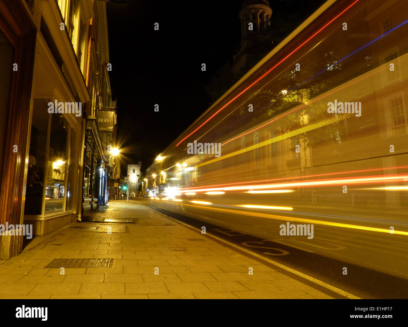 Una lunga esposizione di un autobus andando lungo un high street di notte lasciando sentieri di luce Foto Stock