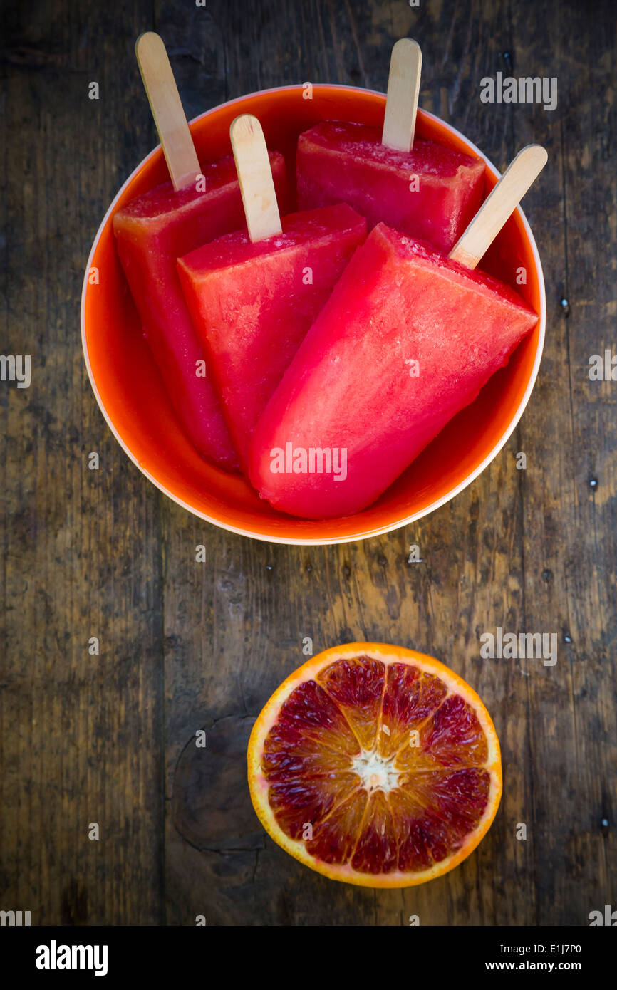 Ciotola di Arancio sanguigno ghiaccioli e fetta di arancia rossa sul legno scuro Foto Stock