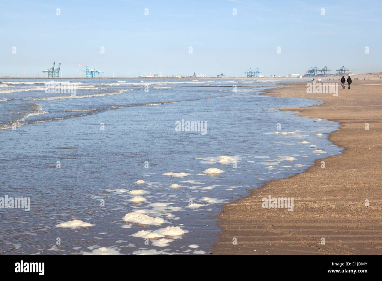 Vista in lontananza matura per passeggiare sulla spiaggia con gru portuali sull orizzonte, Ostenda, Belgio Foto Stock