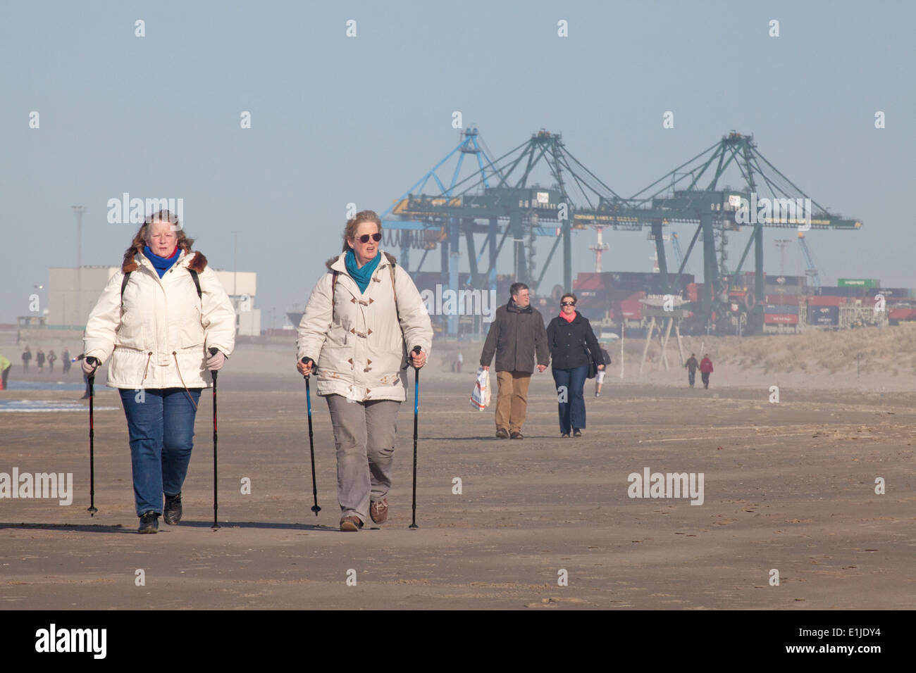 Persone che passeggiano sulla spiaggia con gru portuali sull orizzonte, Zeebrugge, Belgio Foto Stock