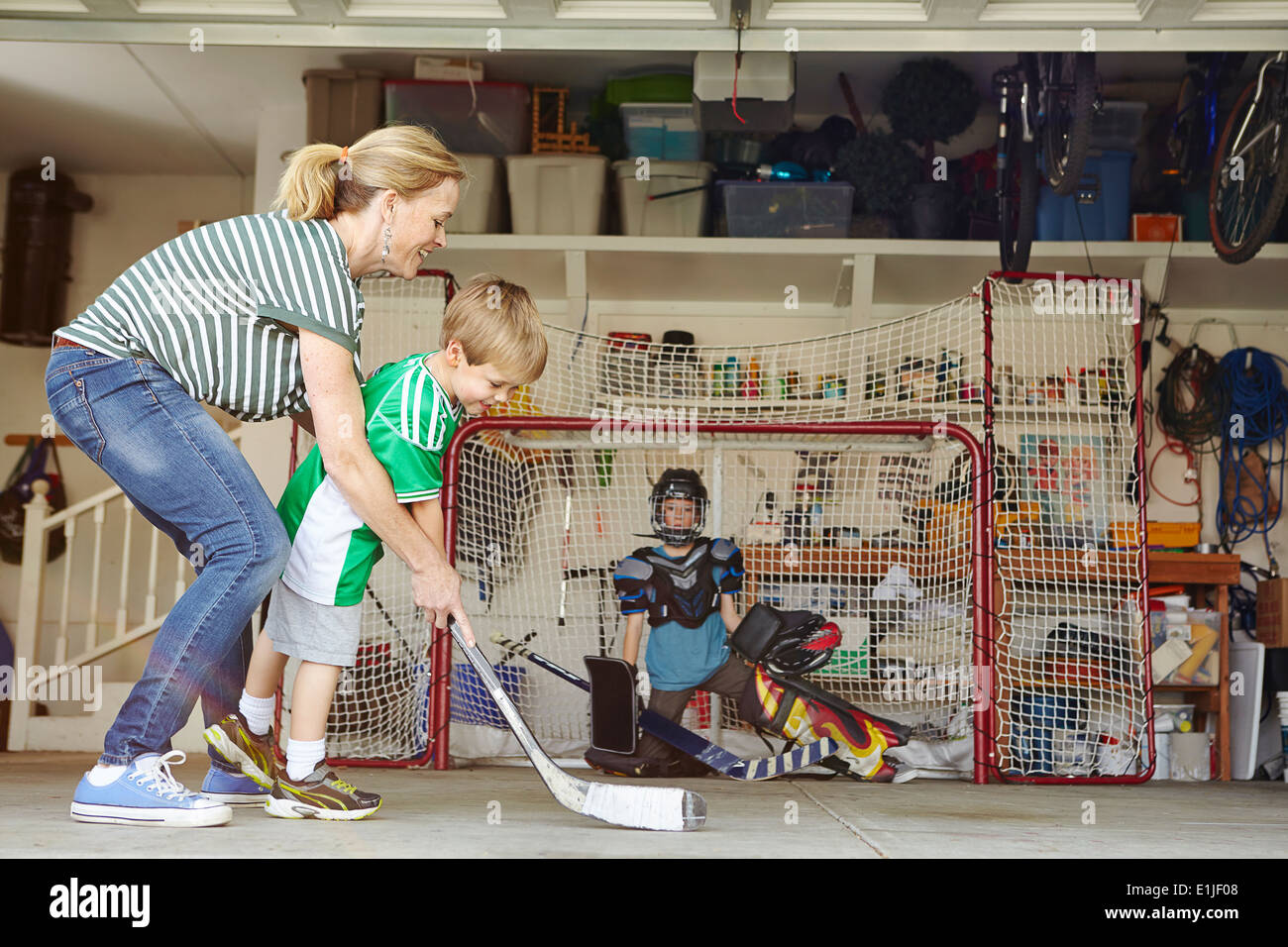 Madre giocare ad hockey in garage con due figli Foto Stock