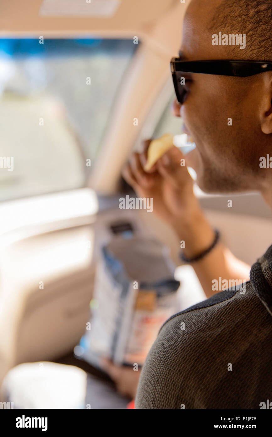 Chiusura del giovane uomo lettura snacking su patatine in auto Foto Stock