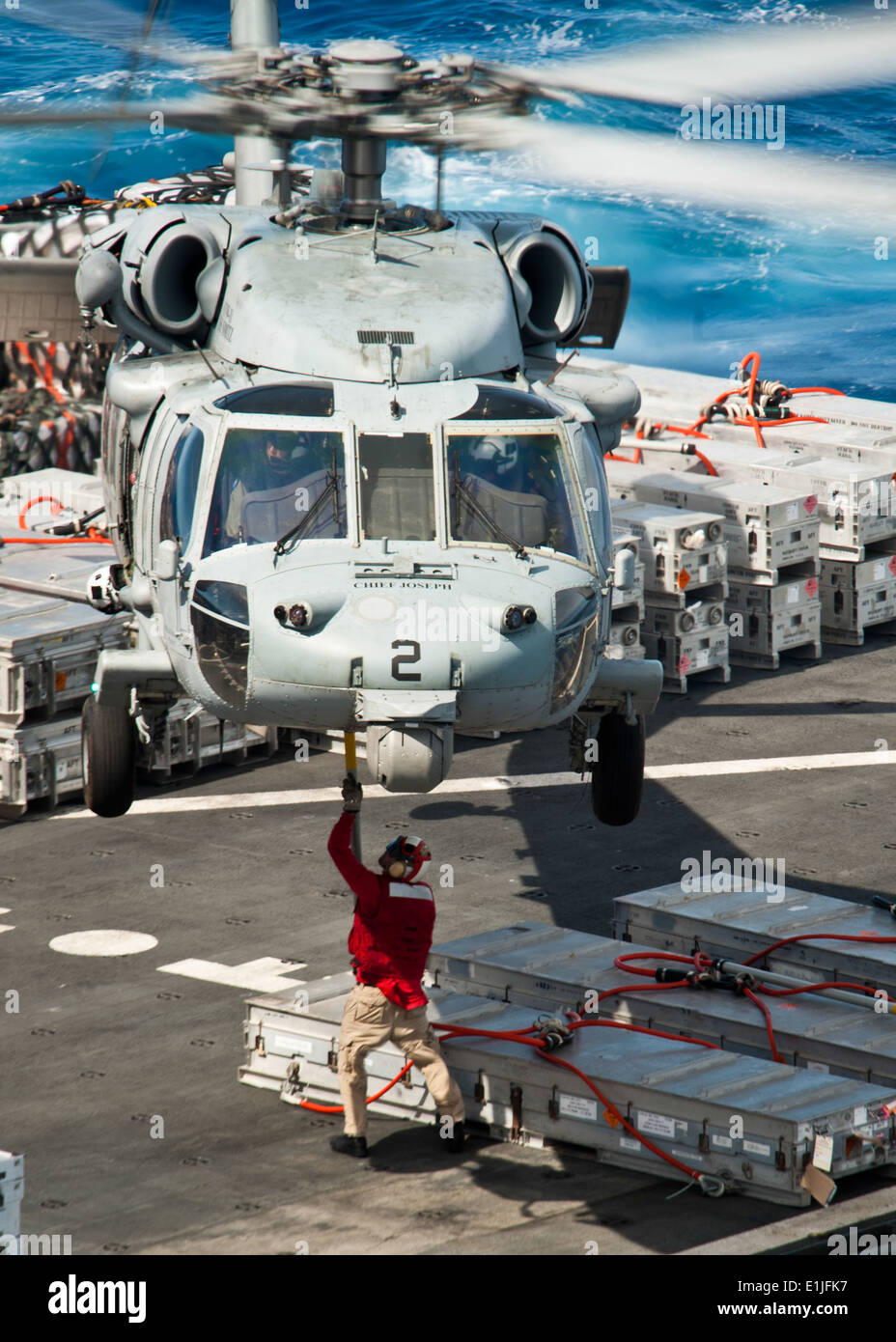 Un membro dell'equipaggio a bordo del trasporto di carichi secchi e munizioni nave USNS Richard E. Byrd (T-AKE 4) attribuisce un gancio di carico ad un MH-60S Seahawk Foto Stock