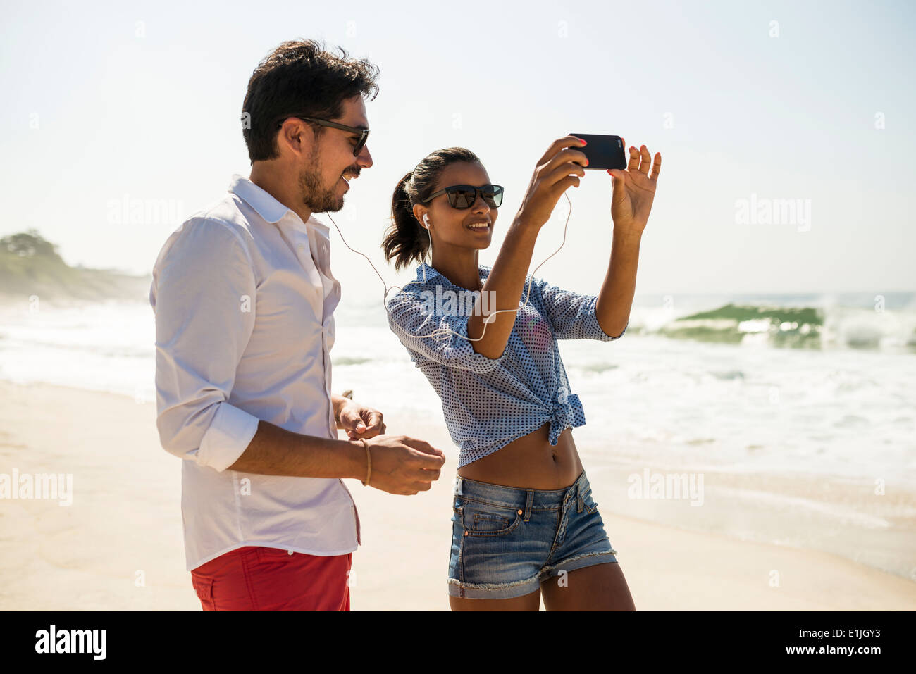 Paio di condividere musica dallo smartphone, Arpoador beach, Rio de Janeiro, Brasile Foto Stock