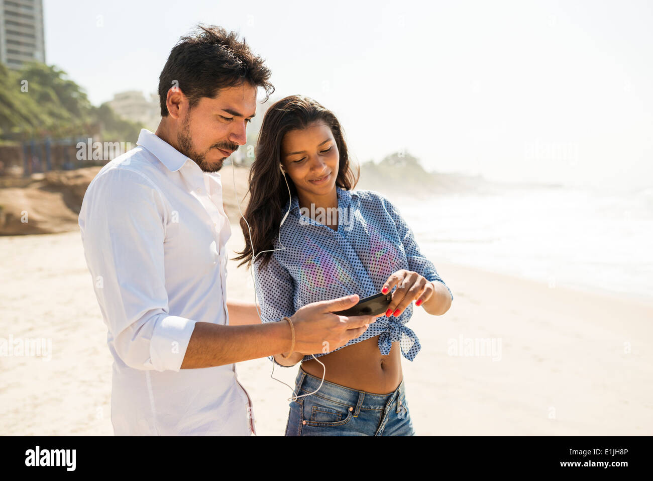 Giovane scegliendo la musica dallo smartphone, Arpoador beach, Rio de Janeiro, Brasile Foto Stock