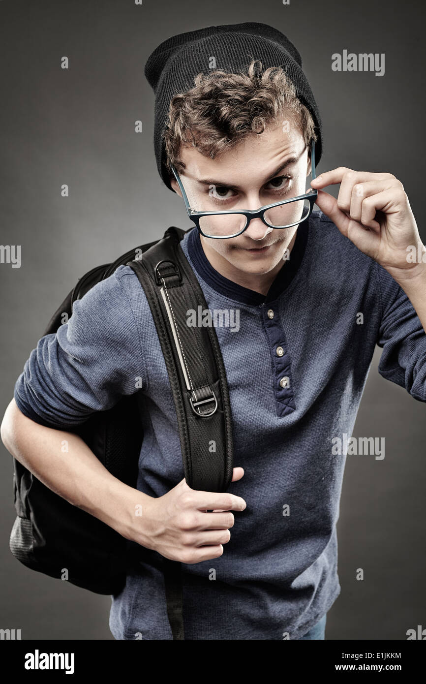 Studio shot del trendy bello ragazzo con zaino guardando sopra gli occhiali Foto Stock