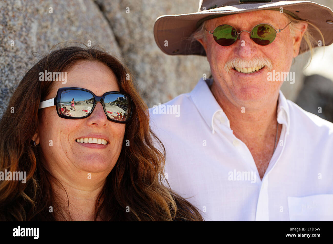 Coppia sorridente in spiaggia indossando occhiali da sole Foto Stock