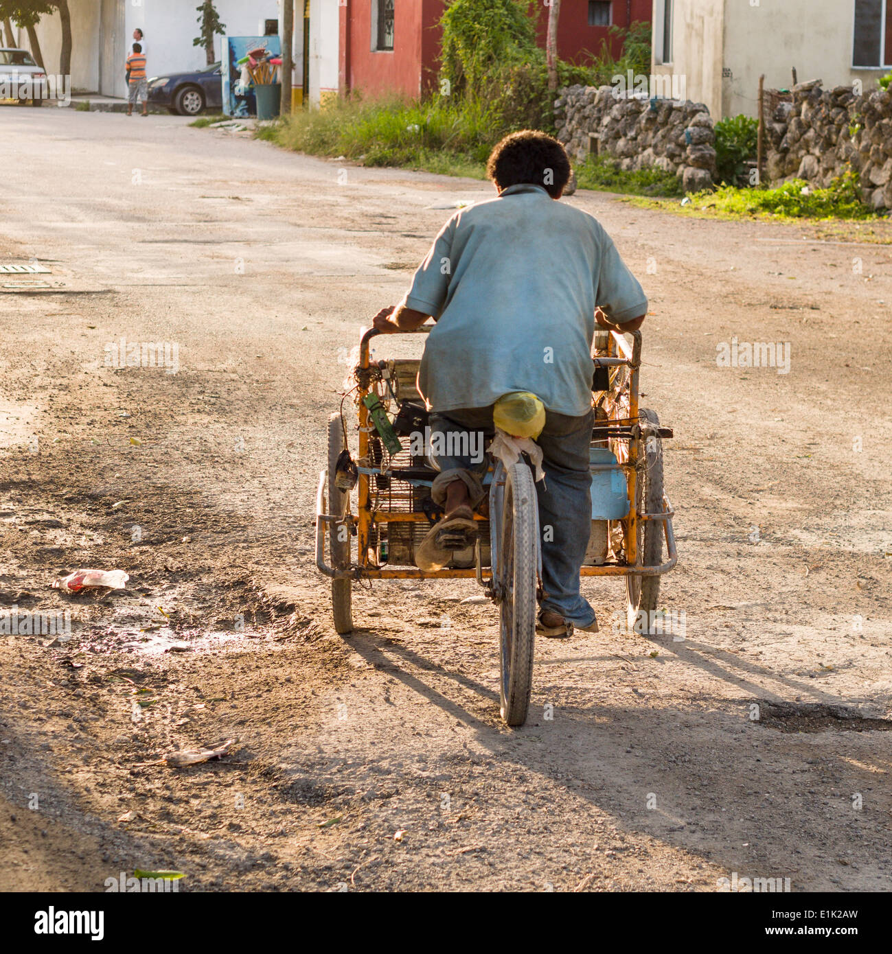 Tornando a casa dopo il lavoro. Una bicicletta caric il sistemaare vendor in flip flop, schivato buche su una strada posteriore a Tulum. Foto Stock