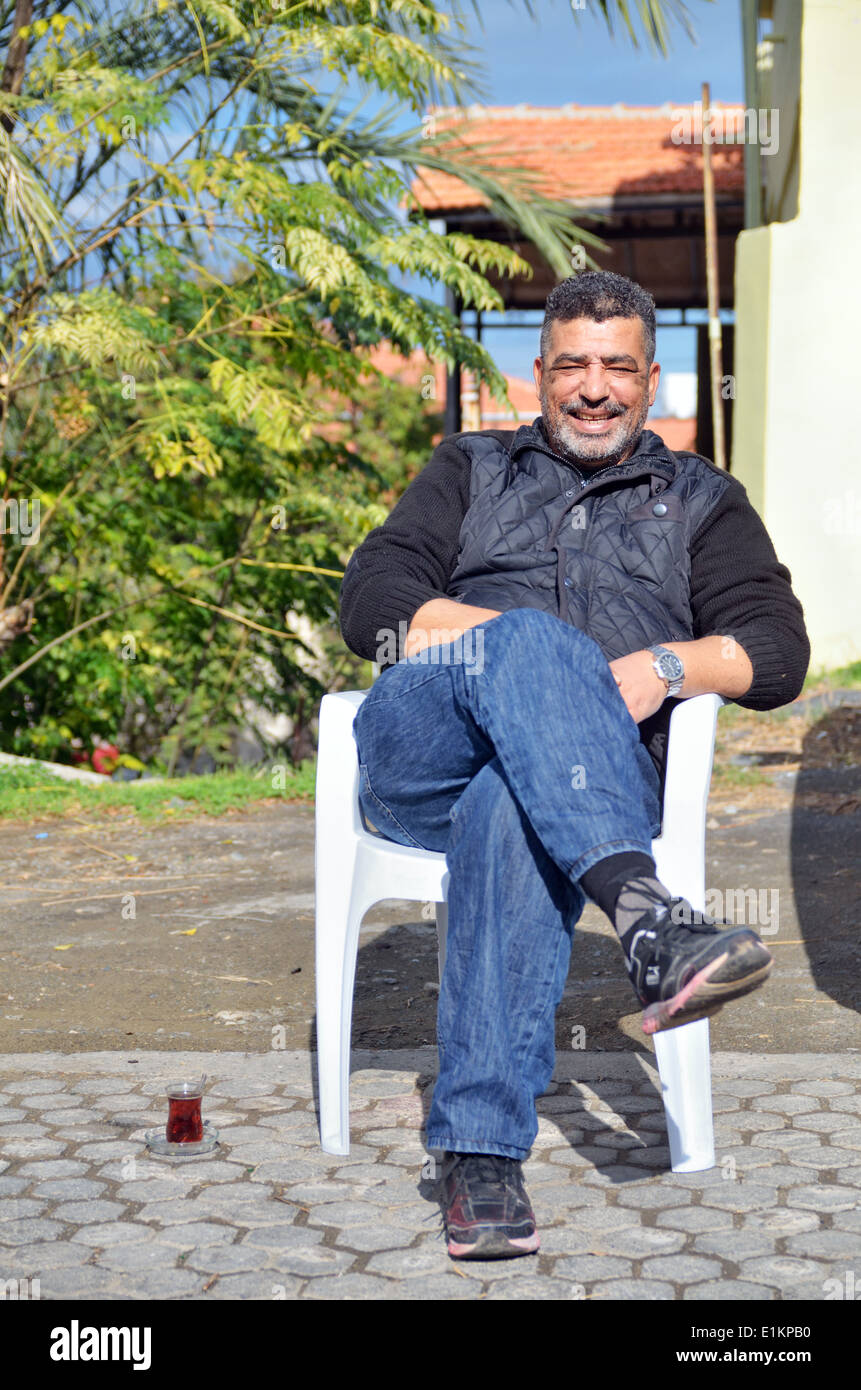 Uomo con tè seduto nella sedia sulla strada e sorridente in Lefka, la parte settentrionale di Cipro Foto Stock