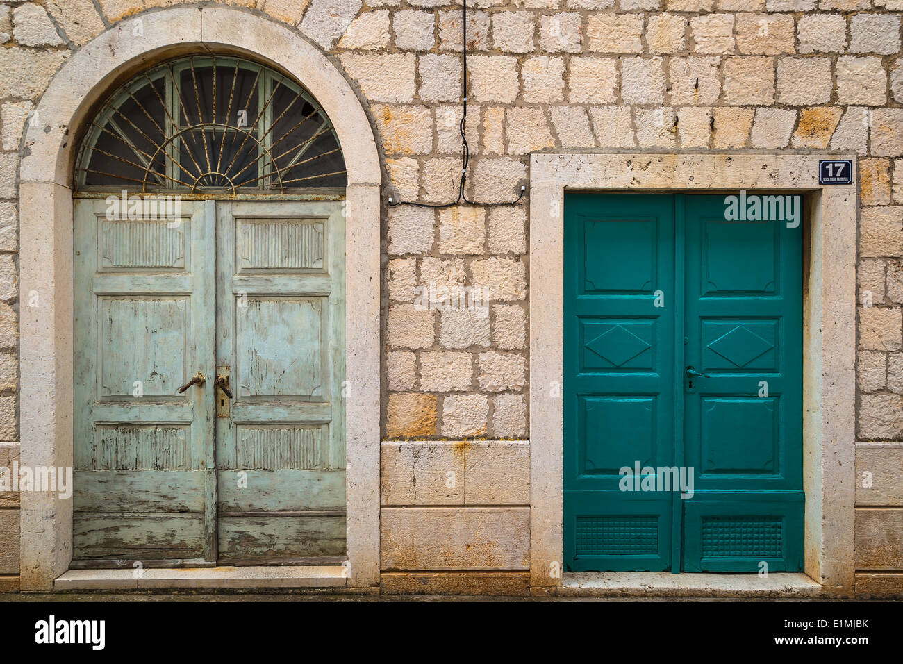 La nuova e la vecchia porta in un muro di pietra mostrano giustapposizione tra la vecchia vernice con ferro forgiato e una nuova porta con vernice fresca Foto Stock