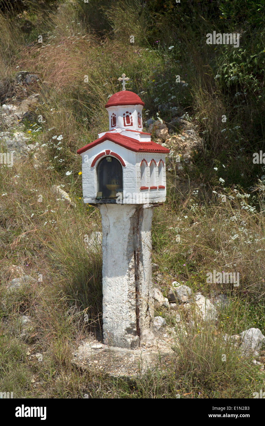 Un rosso e bianco santuario sul ciglio della strada si erge tra fiori selvatici nella vecchia Skala, Cefalonia. Foto Stock