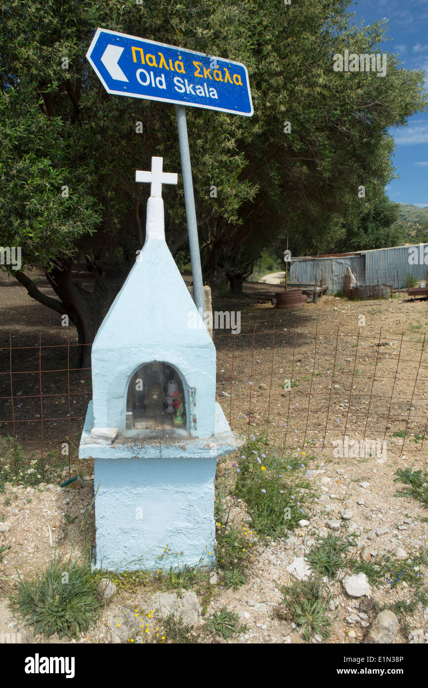 Un santuario sul ciglio della strada si erge di fronte a una strada greca puntando al vecchio Skala, Cefalonia. Foto Stock