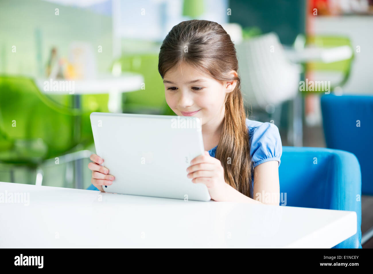 Poco sorridente ragazza seduta alla scrivania e guardando su un marchio nuovo Apple iPad aria Foto Stock
