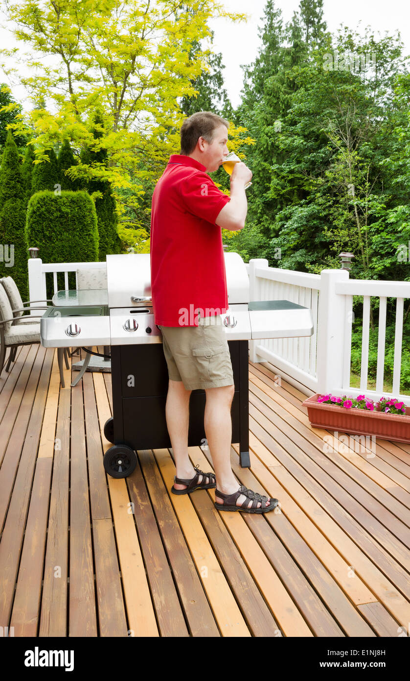 Uomo maturo di bere birra durante la cottura su barbecue Foto Stock