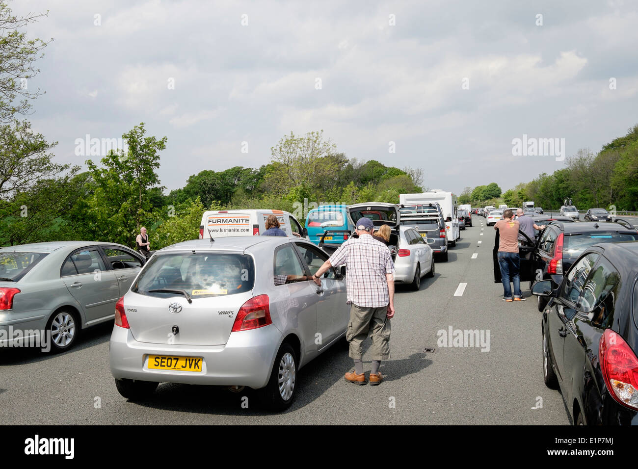 Persone in piedi sulla carreggiata della strada al di fuori di veicoli fermi in coda in un ingorgo di automobili su M6 a causa di un incidente causando lunghi ritardi. Inghilterra, Regno Unito Foto Stock