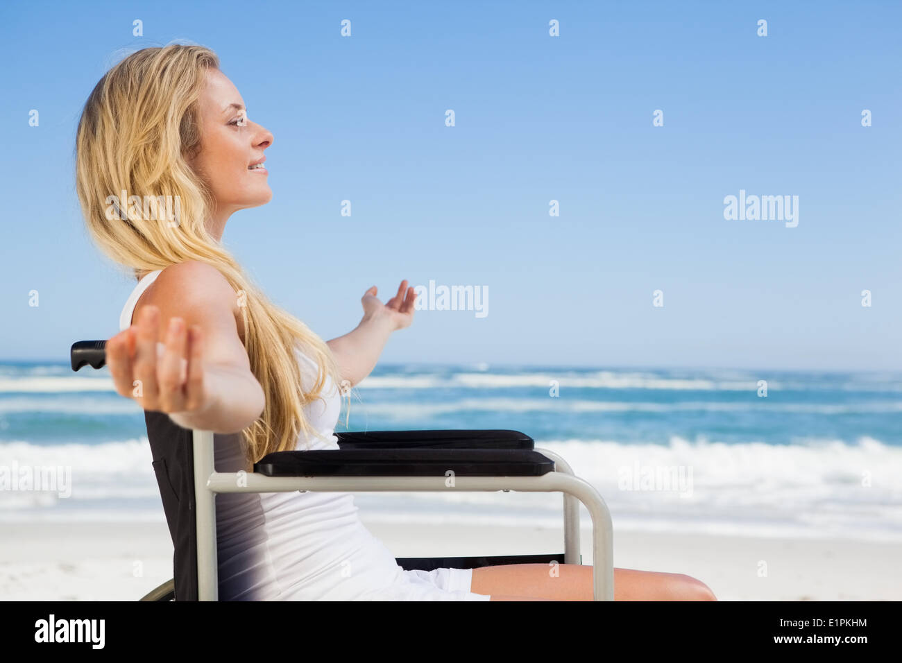 Sedia a rotelle legato bionda sorridente sulla spiaggia Foto Stock
