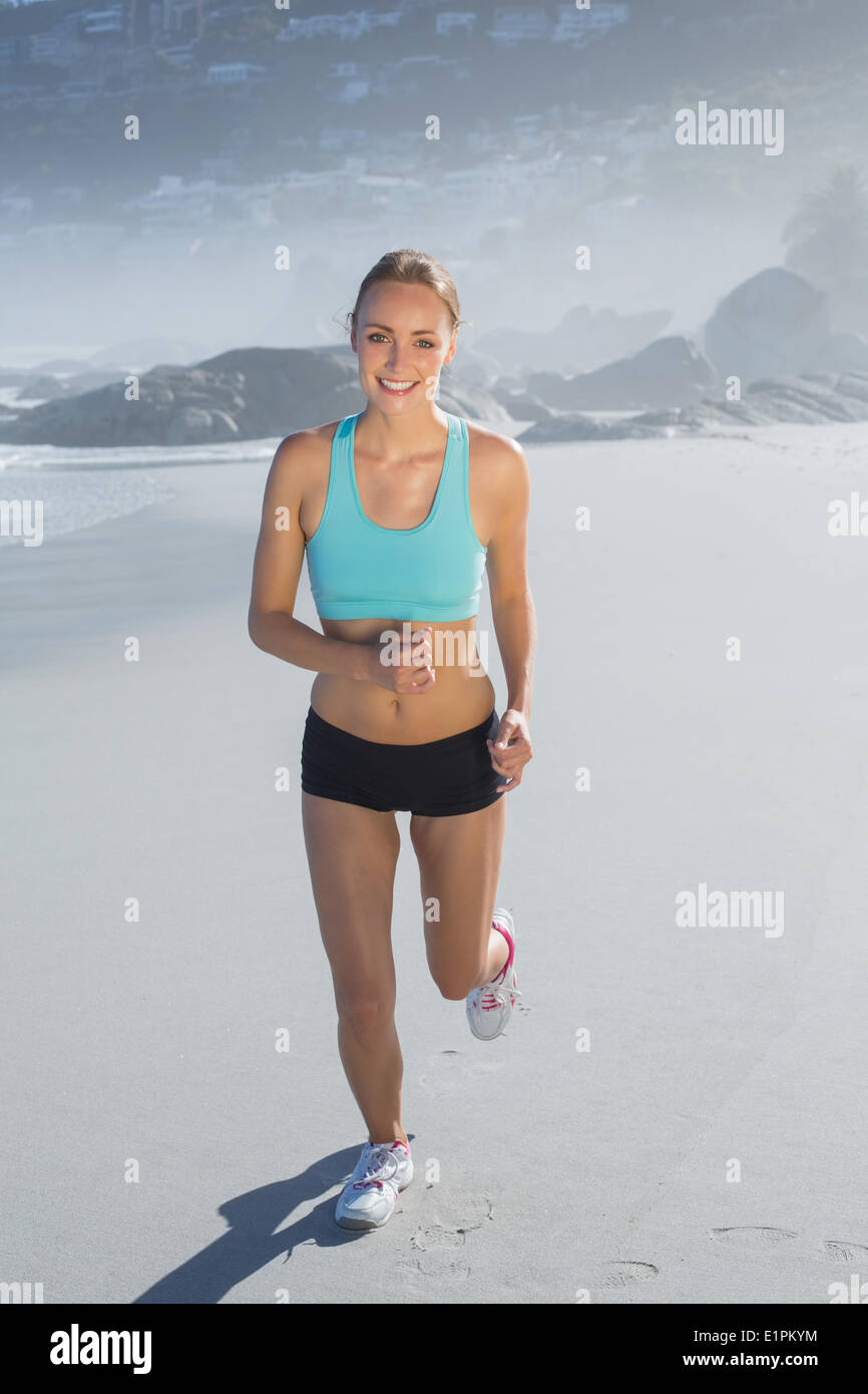 Montare donna sorridente e jogging sulla spiaggia Foto Stock