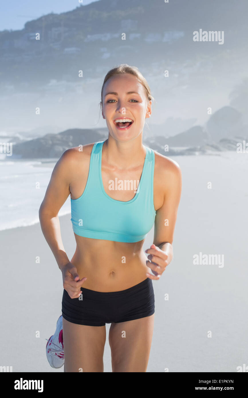 Montare donna sorridente e jogging sulla spiaggia Foto Stock