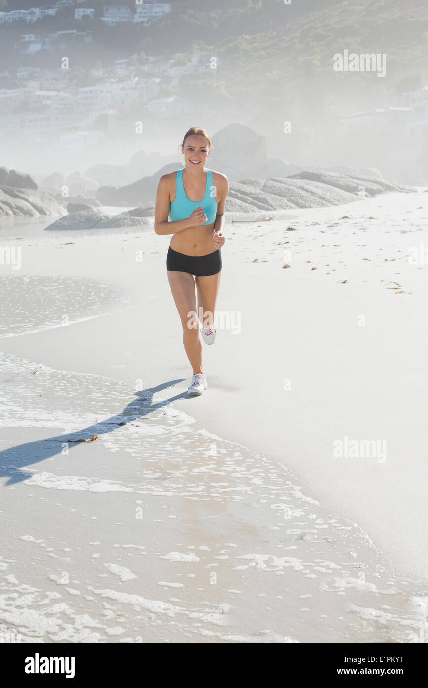 Montare donna jogging sulla spiaggia sorridente in telecamera Foto Stock