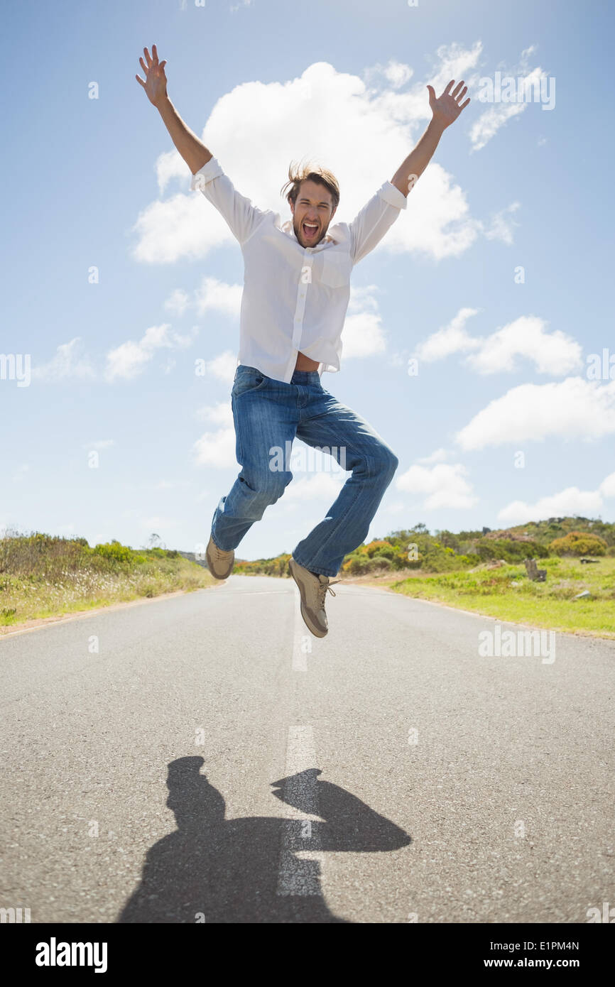 Bel uomo informale saltando su una strada sorridente in telecamera Foto Stock