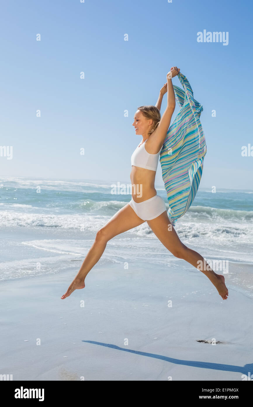 Montare splendida bionda saltando dal mare con sciarpa Foto Stock