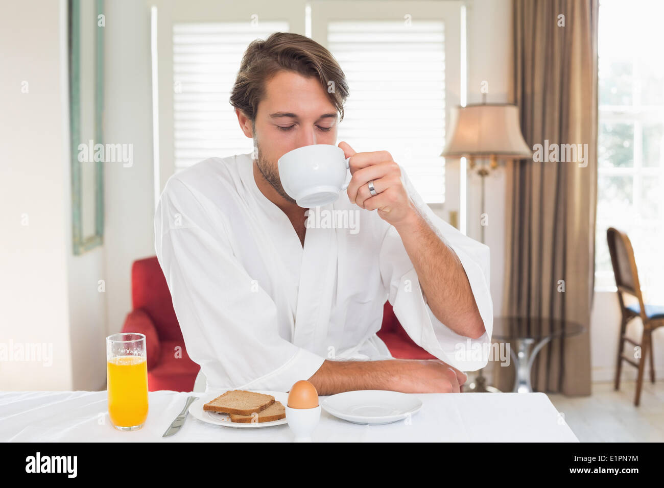 Uomo bello avere la prima colazione nel suo accappatoio di bere il caffè Foto Stock