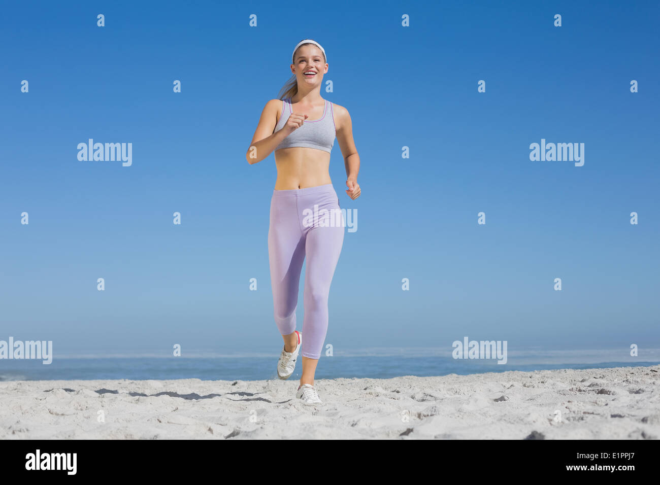 Bionda sportiva sulla spiaggia jogging verso la telecamera Foto Stock