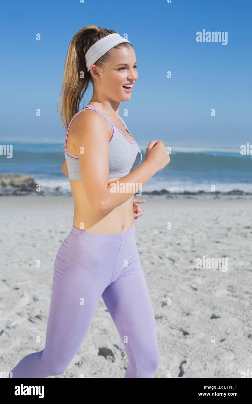 Sportivo bionda sorridente jogging sulla spiaggia Foto Stock