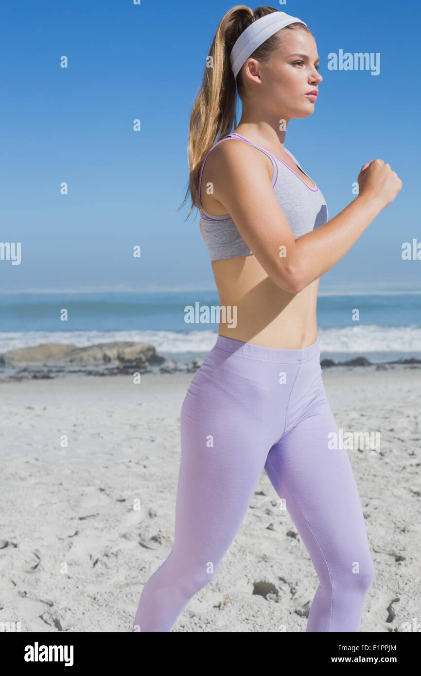 Sporty focalizzata bionda jogging sulla spiaggia Foto Stock