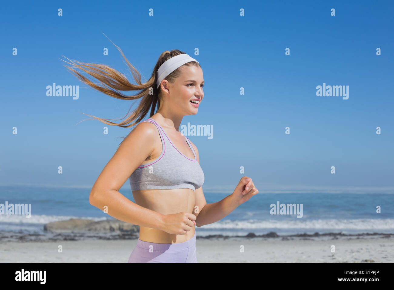 Sportivo bionda sorridente jogging sulla spiaggia Foto Stock