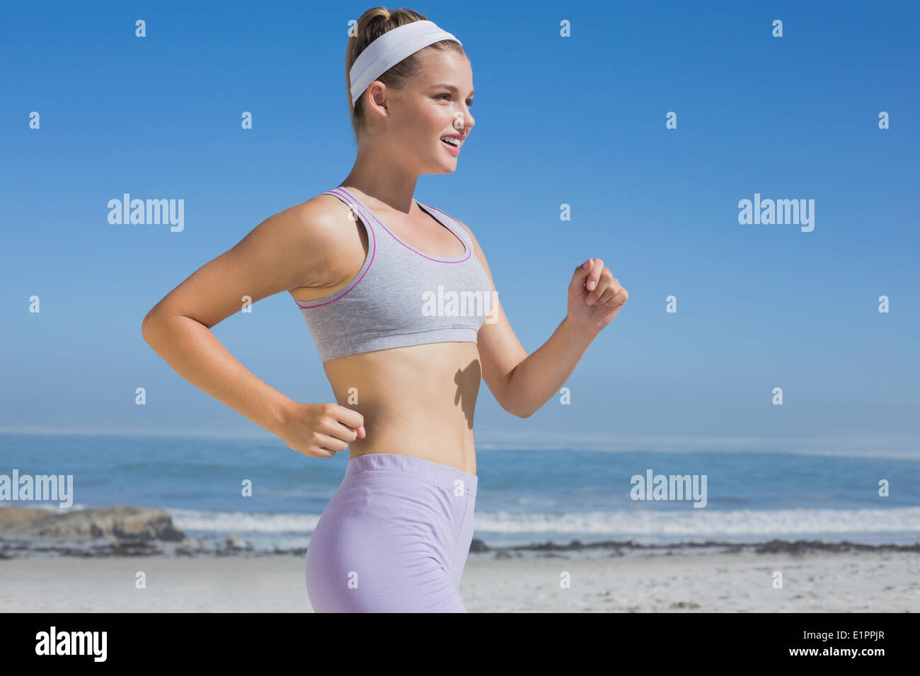 Sportivo bionda sorridente jogging sulla spiaggia Foto Stock