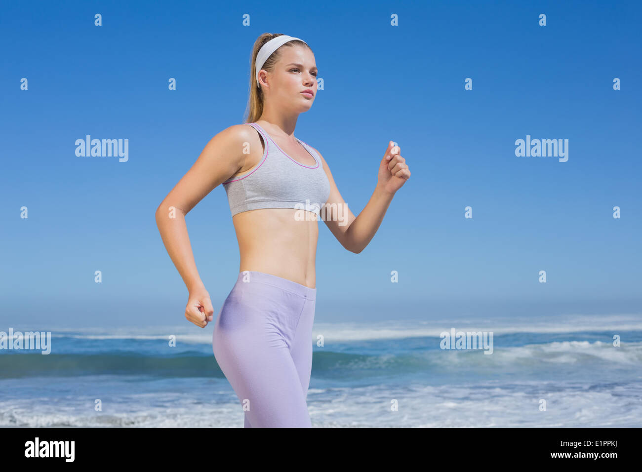 Sporty focalizzata bionda jogging sulla spiaggia Foto Stock