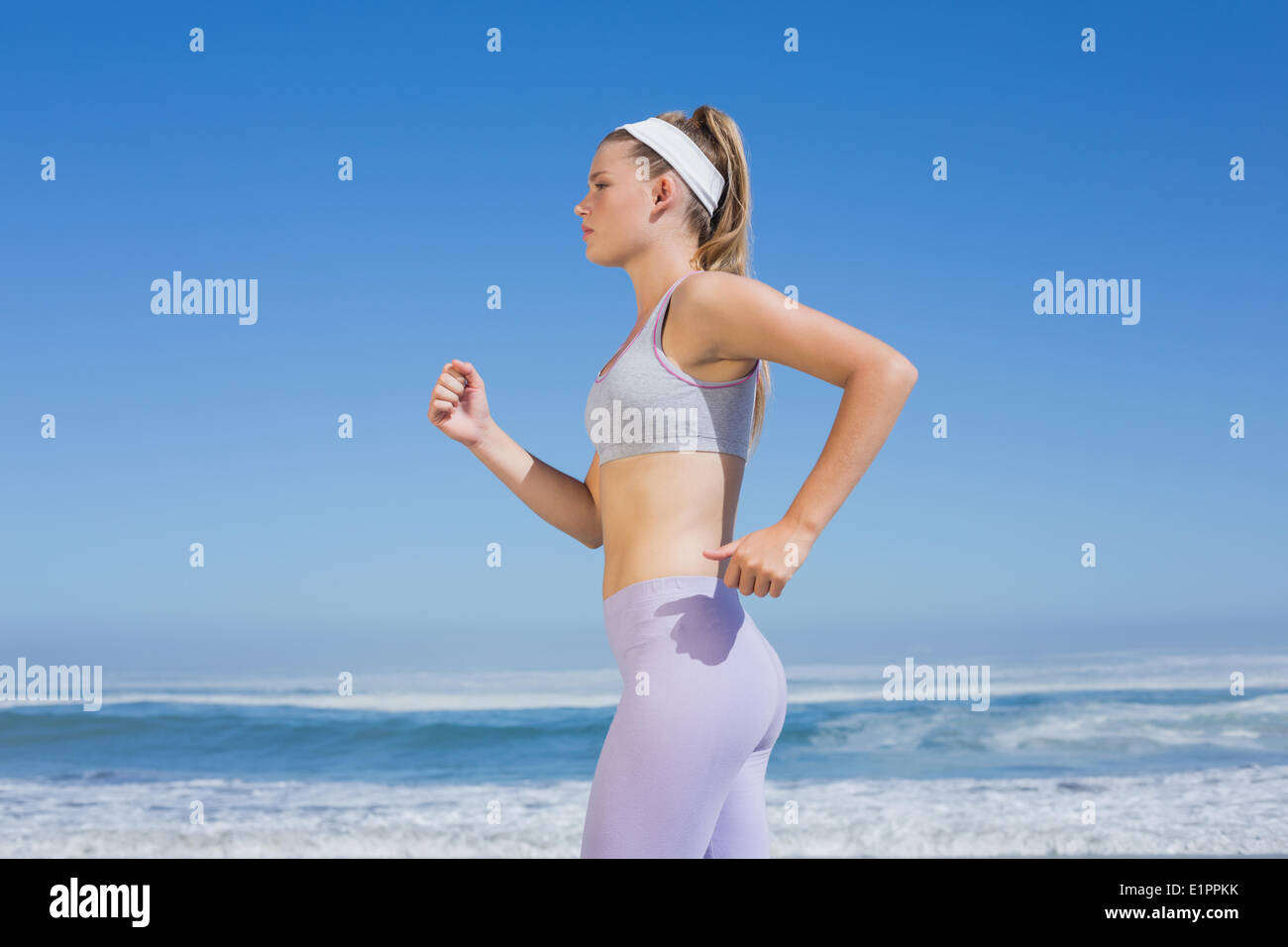 Sporty focalizzata bionda jogging sulla spiaggia Foto Stock