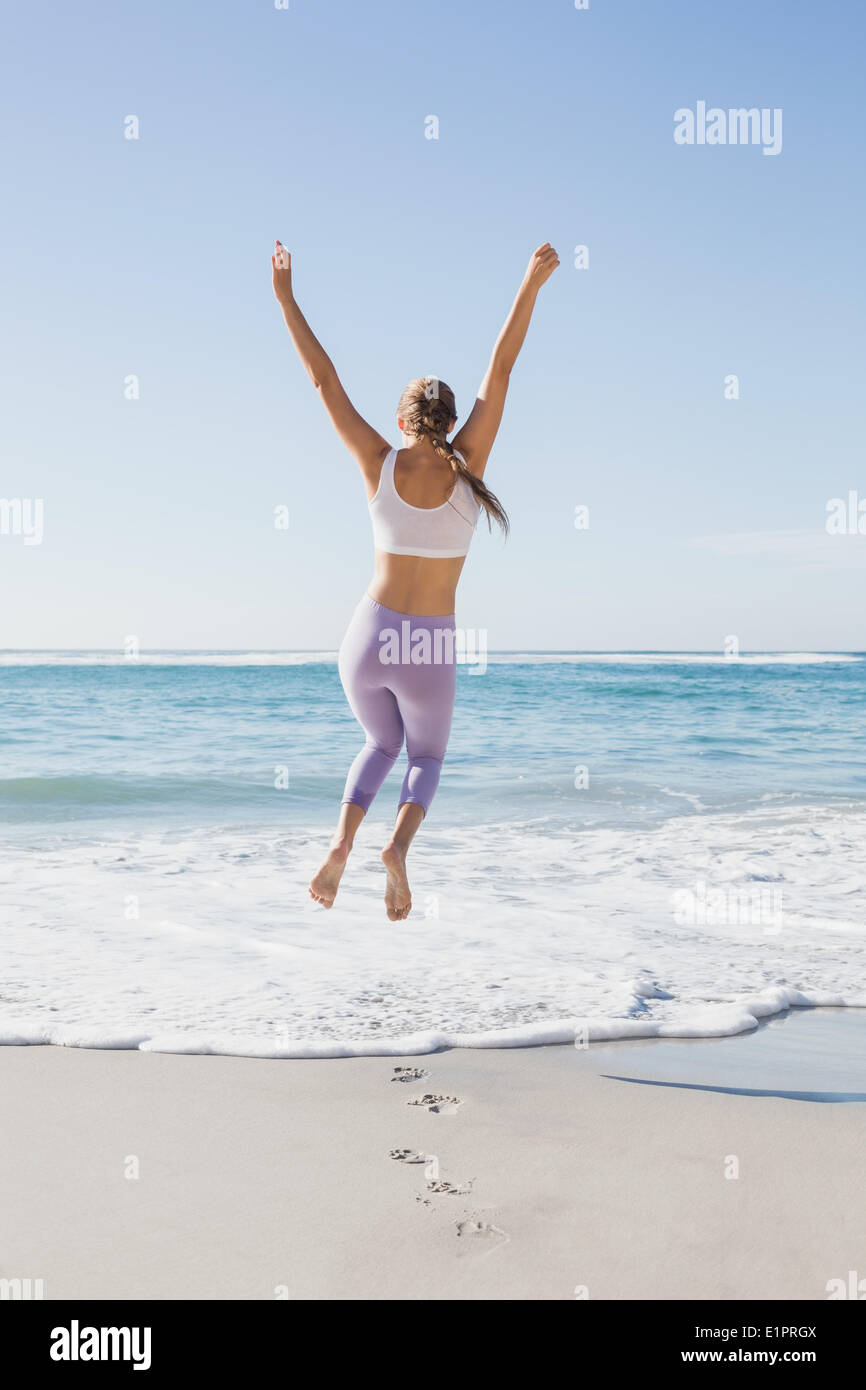 Sporty blonde jumping fino sulla spiaggia Foto Stock