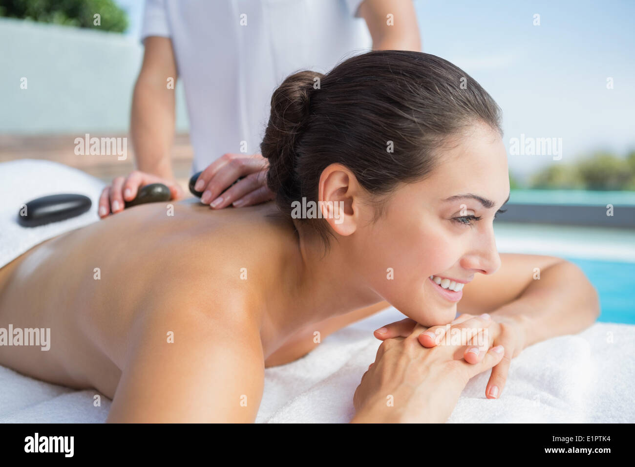 Happy brunette ottenendo un massaggio hot stone a bordo piscina Foto Stock