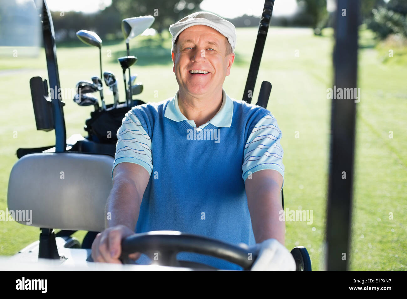 Felice golfista alla guida della sua golf buggy sorridente in telecamera Foto Stock
