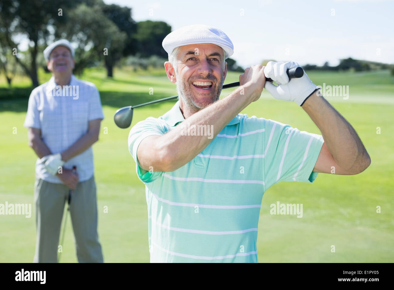 Il Golfer oscillando la sua club con amico dietro di lui Foto Stock