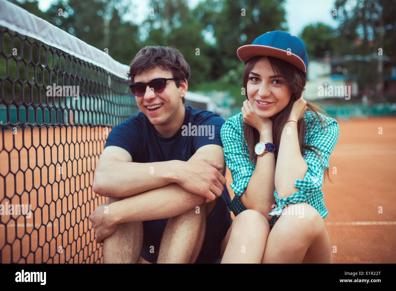Giovane bella giovane seduto su uno skateboard sul campo da tennis Foto Stock