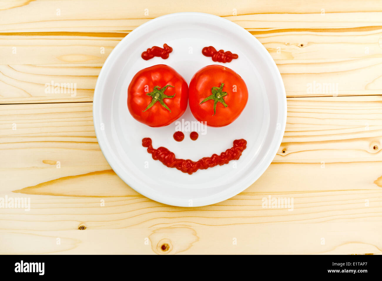 Divertimento e alimenti per bambini - pomodori e ketchup rendendo Smiley face servita su una piastra bianca sul tavolo di legno. Foto Stock