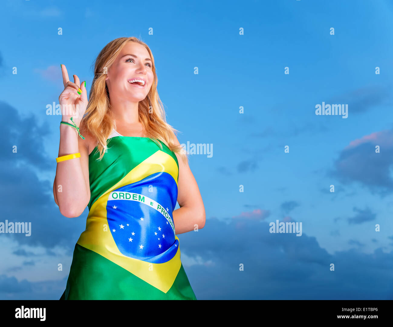 Felice fan del calcio brasiliano squadra, allegro Pretty girl su stadium il tifo a sostegno, indossando grande bandiera nazionale del Brasile Foto Stock