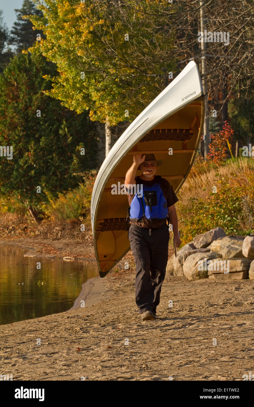 Uomo maturo porta canoa da acqua, Oxtongue Lago, Muskoka, Ontario, Canada. Foto Stock