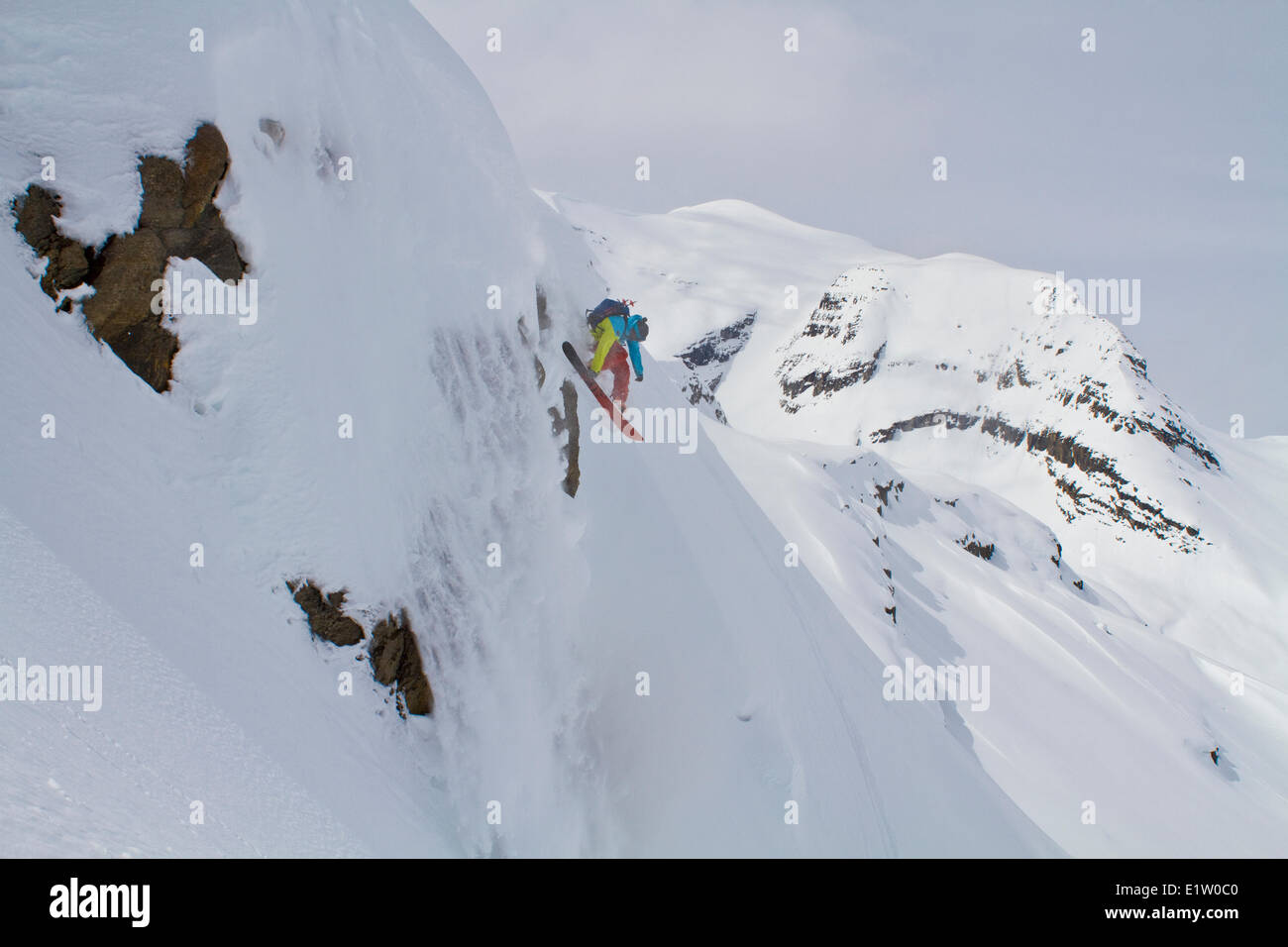 Un maschio splitboarder scende di una scogliera con la sua sluff nelle montagne rocciose canadesi backcountry. Ghiacciaio Lodge, Golden, BC Foto Stock