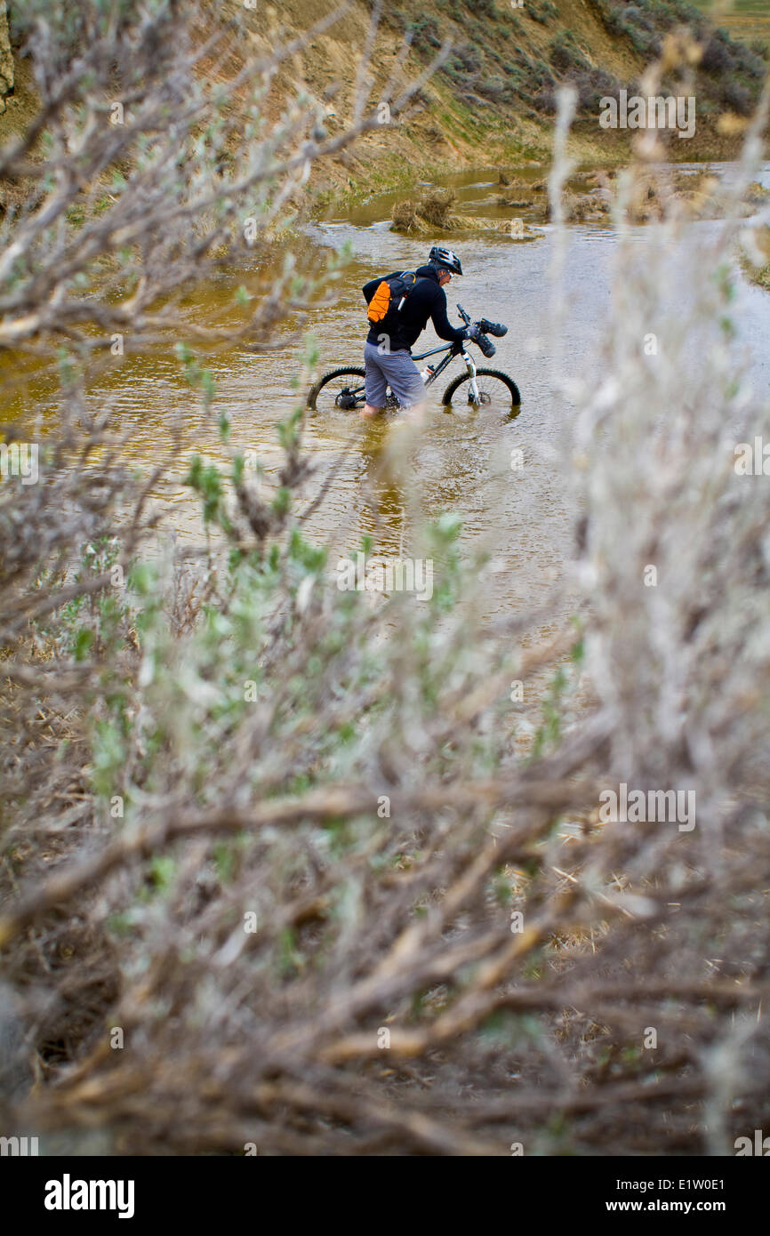 Un uomo spinge la sua mountain bike attraverso la molla run off condizioni sul Maah Daah Hey Trail, North Dakota Foto Stock