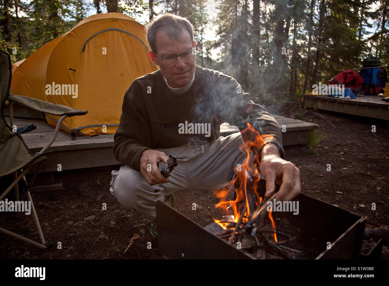 Uomo di mezza età inizia a fuoco in campeggio a Virginia Falls, Parco Nazionale Nahanni preservare, NWT, Canada. Foto Stock