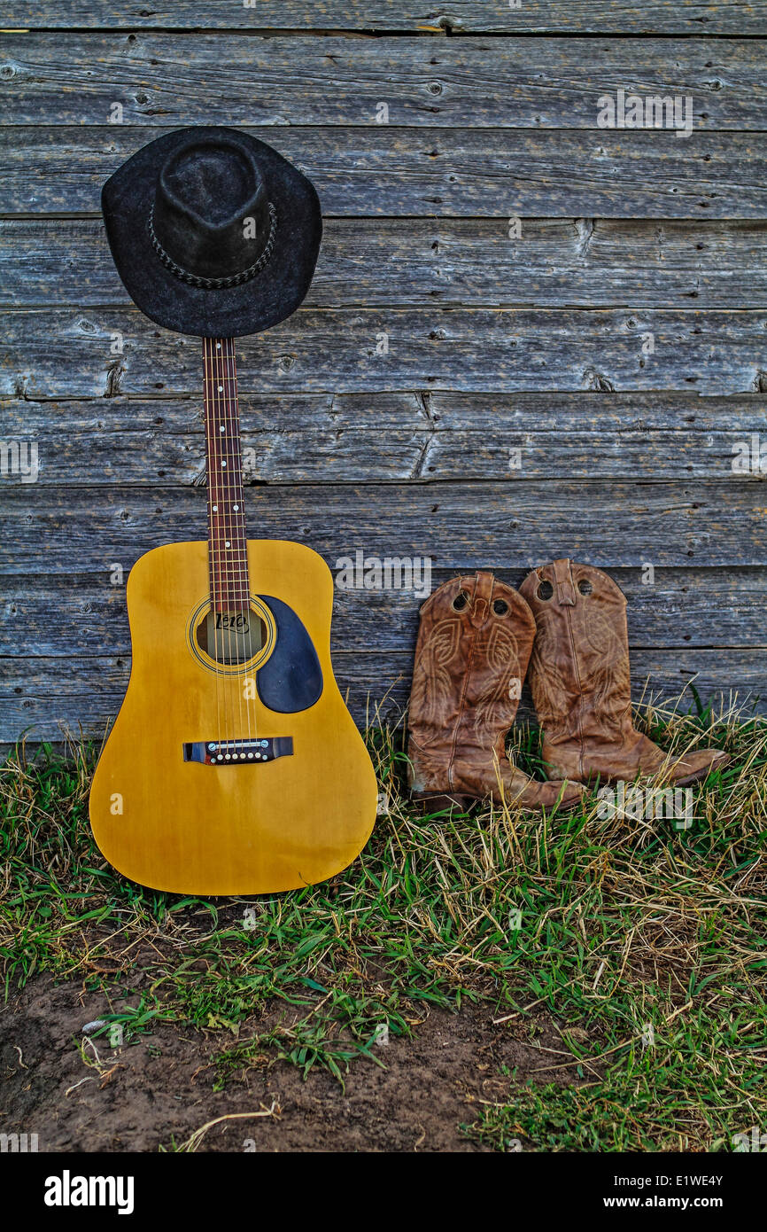 Acoutic guitar, cappello da cowboy, stivali da cowboy e vecchio, invecchiato farm shed parete. Rural Alberta, Canada. Foto Stock